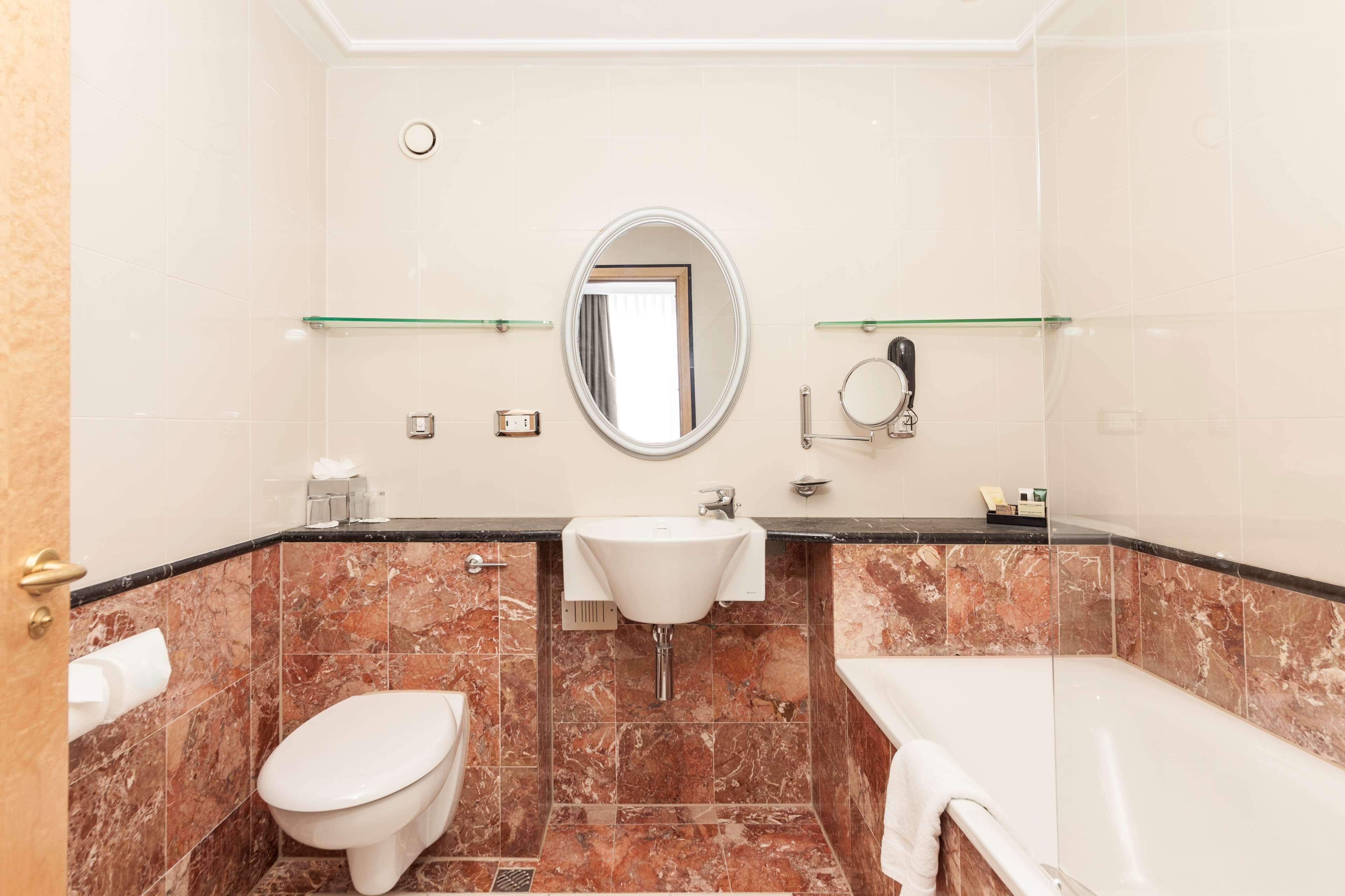 A bathroom with a toilet, sink, and bathtub, marble tiles, and a mirror.