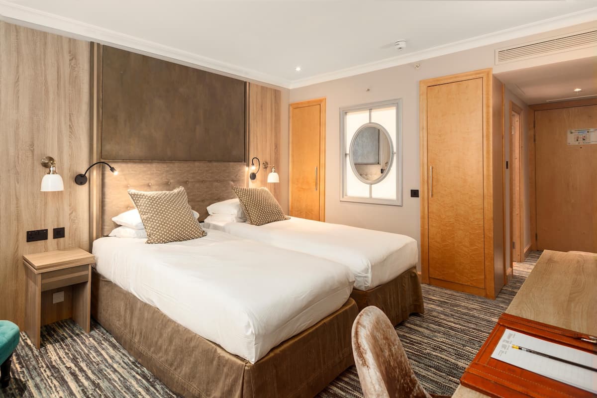 Ein Hotelzimmer mit zwei Betten, einem Schreibtisch, einem Stuhl, einem Spiegel und einem Kleiderschrank.