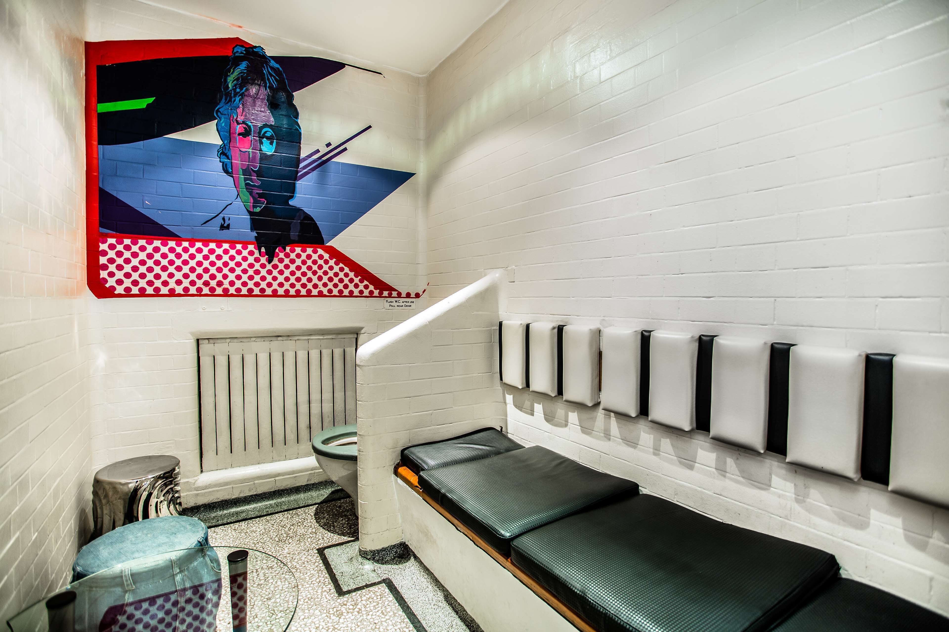 A room with a bench, a radiator, a toilet, and a wall-mounted hand sanitizer dispenser.
