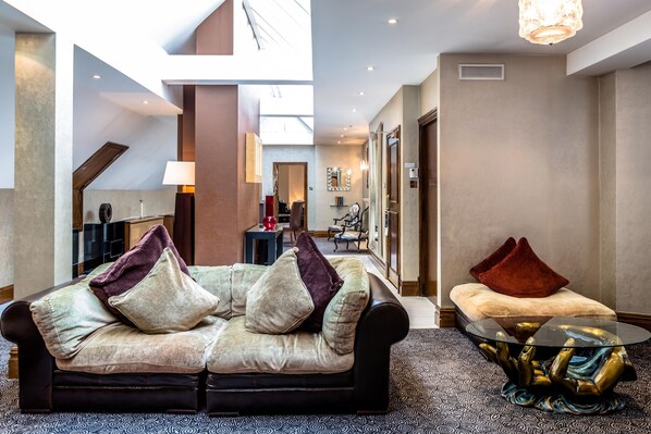 A spacious living area with a sofa, a glass coffee table, and a red accent pillow. - Courthouse Hotel (London)