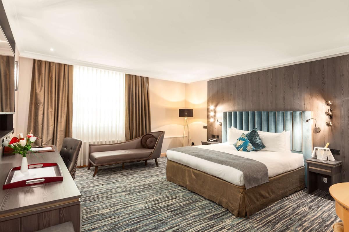 Ein Hotelzimmer mit einem großen Bett, einem Schreibtisch mit Tablett, einem Sessel, einer Lampe und einem Nachttisch.