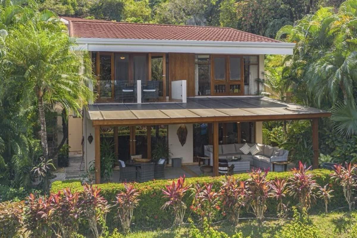 Ein zweistöckiges Haus mit überdachter Terrasse, umgeben von üppiger Vegetation.