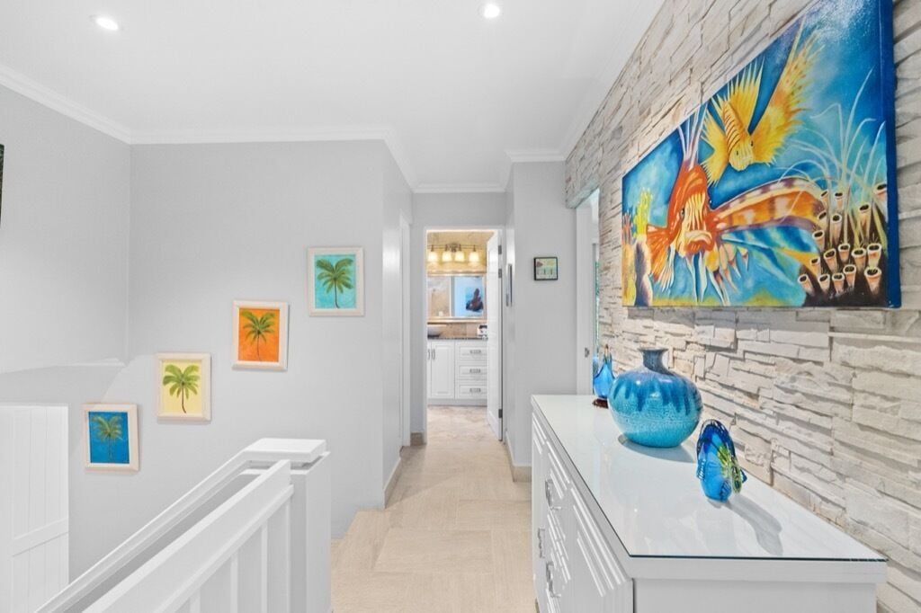A hallway with a staircase, a kitchen in the background, and a wall with a large painting and decorative vases.