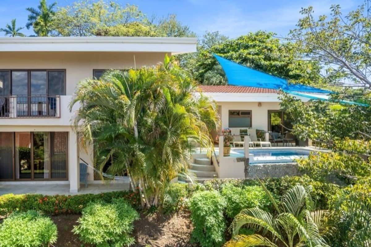 Ein zweistöckiges Haus mit Balkon, Schwimmbad und üppiger Bepflanzung.