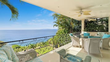 Un balcon avec vue sur la mer, aménagé avec des fauteuils en osier et une table en verre.