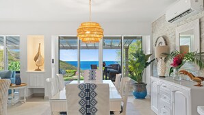 Un espace de restauration moderne avec vue sur la mer, doté de meubles blancs et d’un luminaire suspendu.