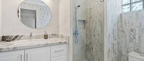 A bathroom with a marble sink, a round mirror, a glass-enclosed shower, and a toilet.