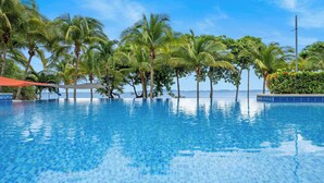 Une piscine à débordement à l’eau d’un bleu cristallin, entourée de palmiers et offrant une vue sur l’océan.