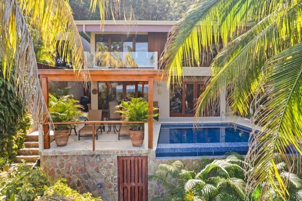 Ein modernes Haus mit Pool, umgeben von üppigen tropischen Pflanzen.