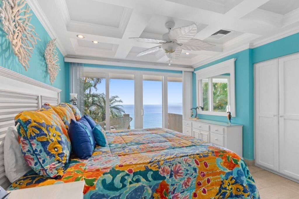 A bedroom with a large bed, a ceiling fan, and a view of the ocean.