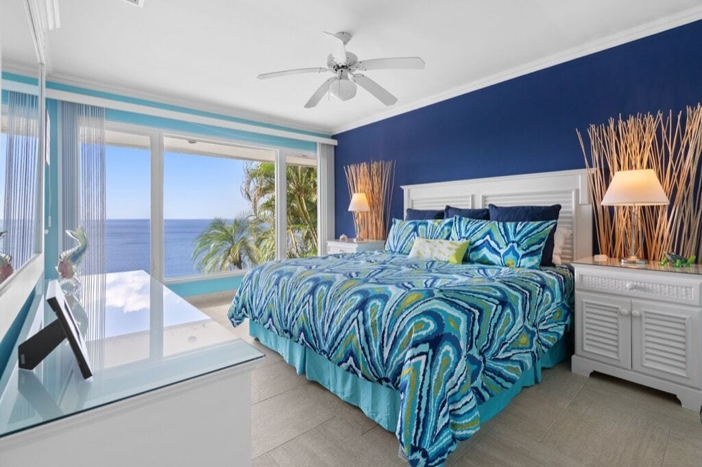 Un dormitorio con una cama grande, un ventilador de techo y vista al océano.