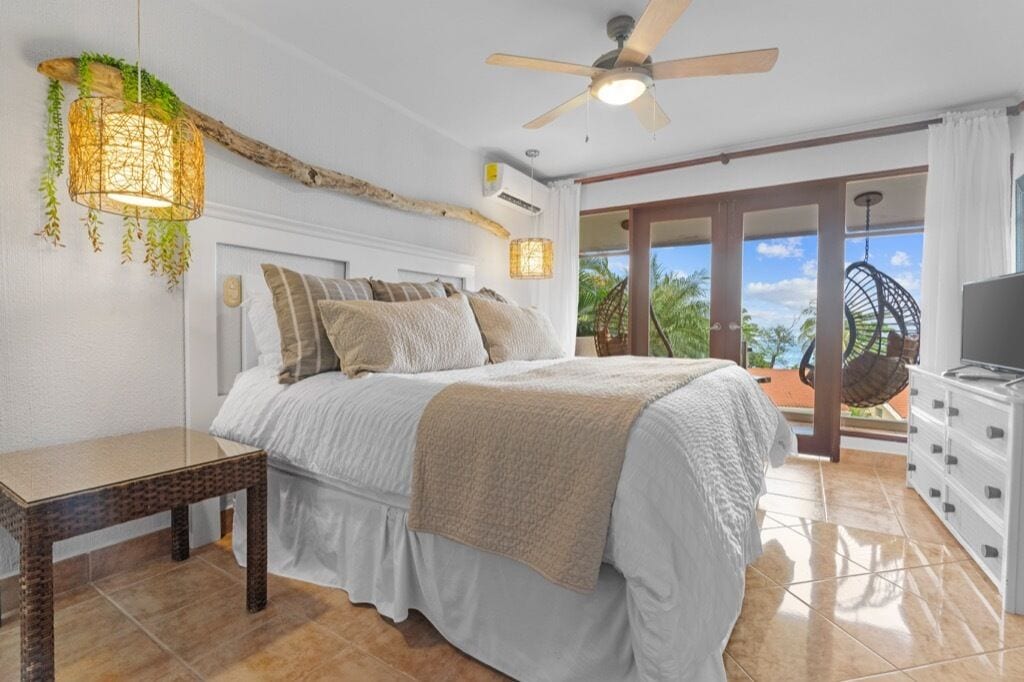 Ein Schlafzimmer mit Bett, Nachttisch, Deckenventilator und Blick ins Freie.