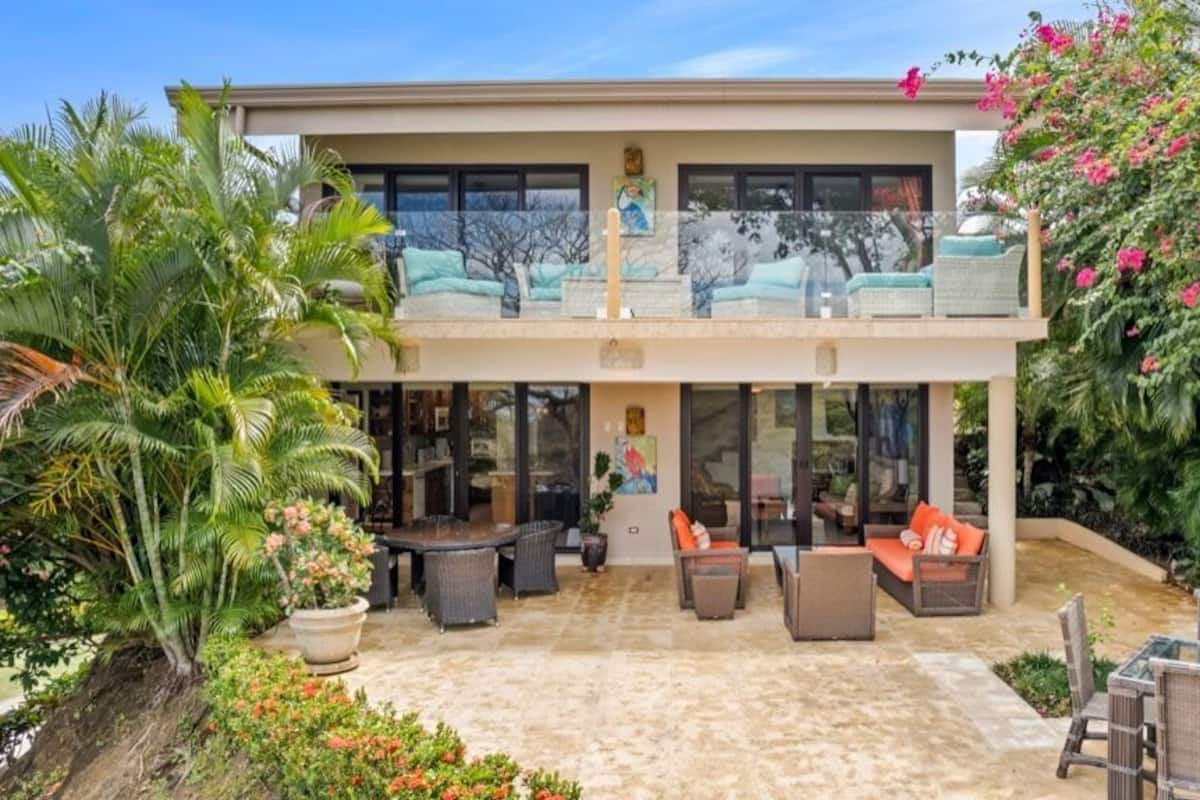 Ein zweistöckiges Haus mit einer Terrassenfläche, die Gartenmöbel und einen großen Blumentopf zeigt.