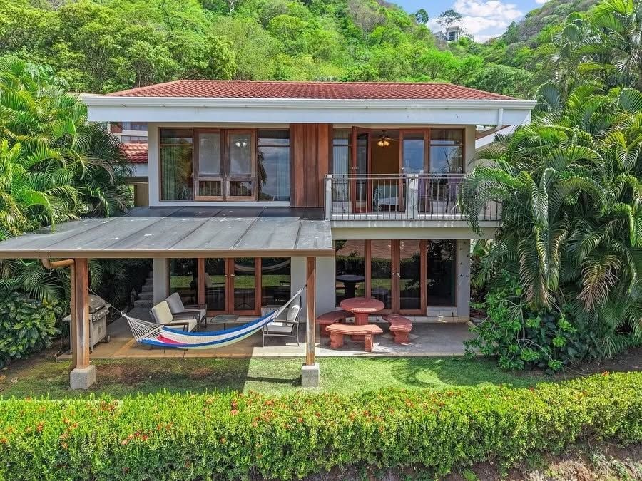A two-story house with a covered patio, outdoor furniture, and a hammock.