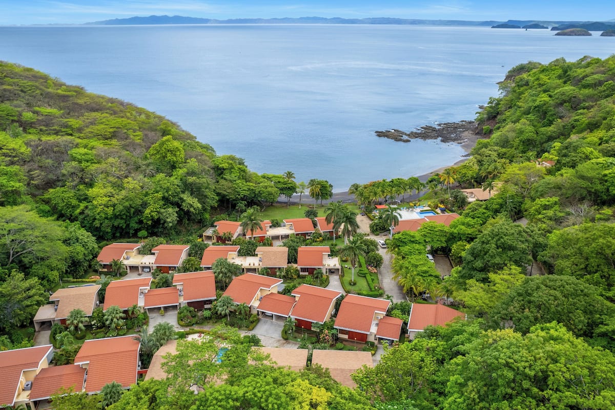 Ein Küstenresort mit mehreren bungalowsähnlichen Gebäuden, einem zentralen Pool und üppiger Vegetation rund um das Anwesen.