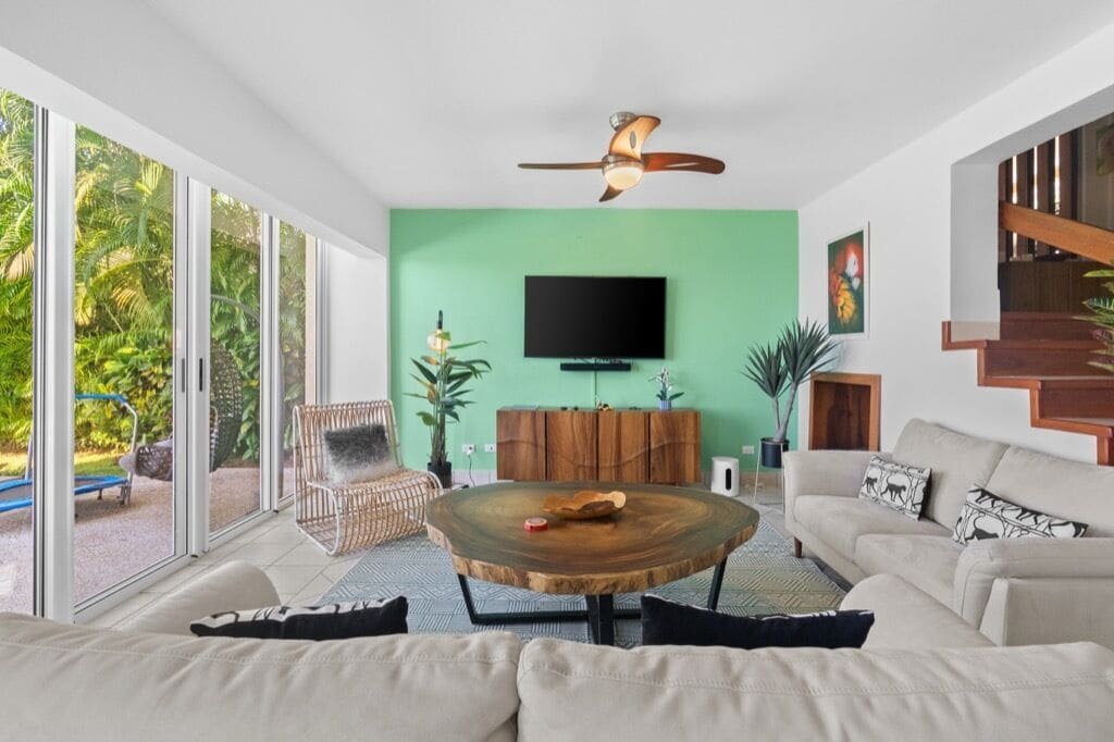 Una sala de estar moderna con un ventanal grande, una mesa redonda de madera, un sofá y un televisor montado en la pared.