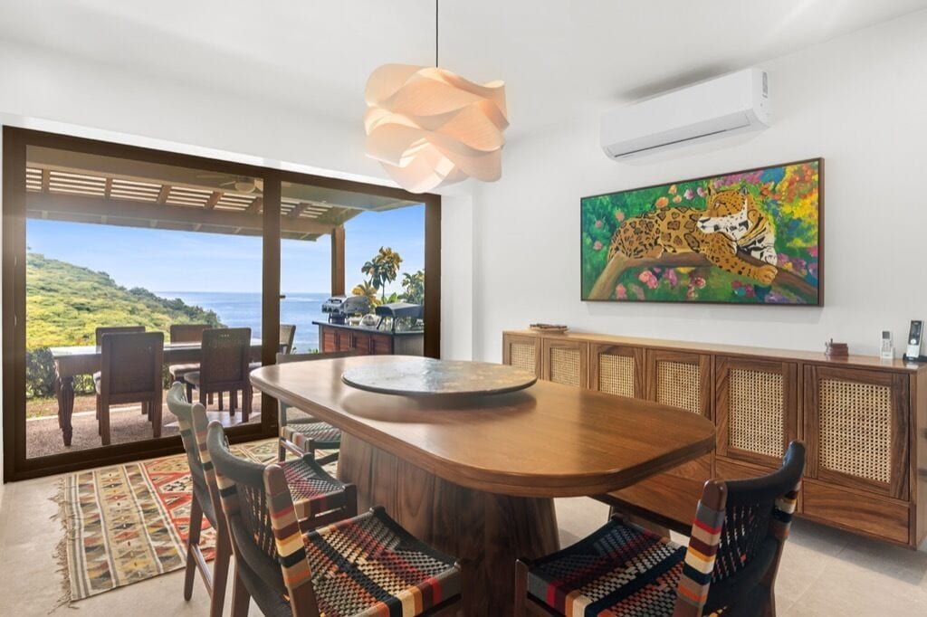 Un espace repas avec une grande table en bois, des chaises en osier et une vue sur l’océan.