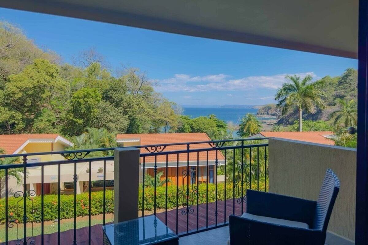 Ein Balkon mit Blick auf eine Küstenlandschaft, darunter Häuser und Palmen.