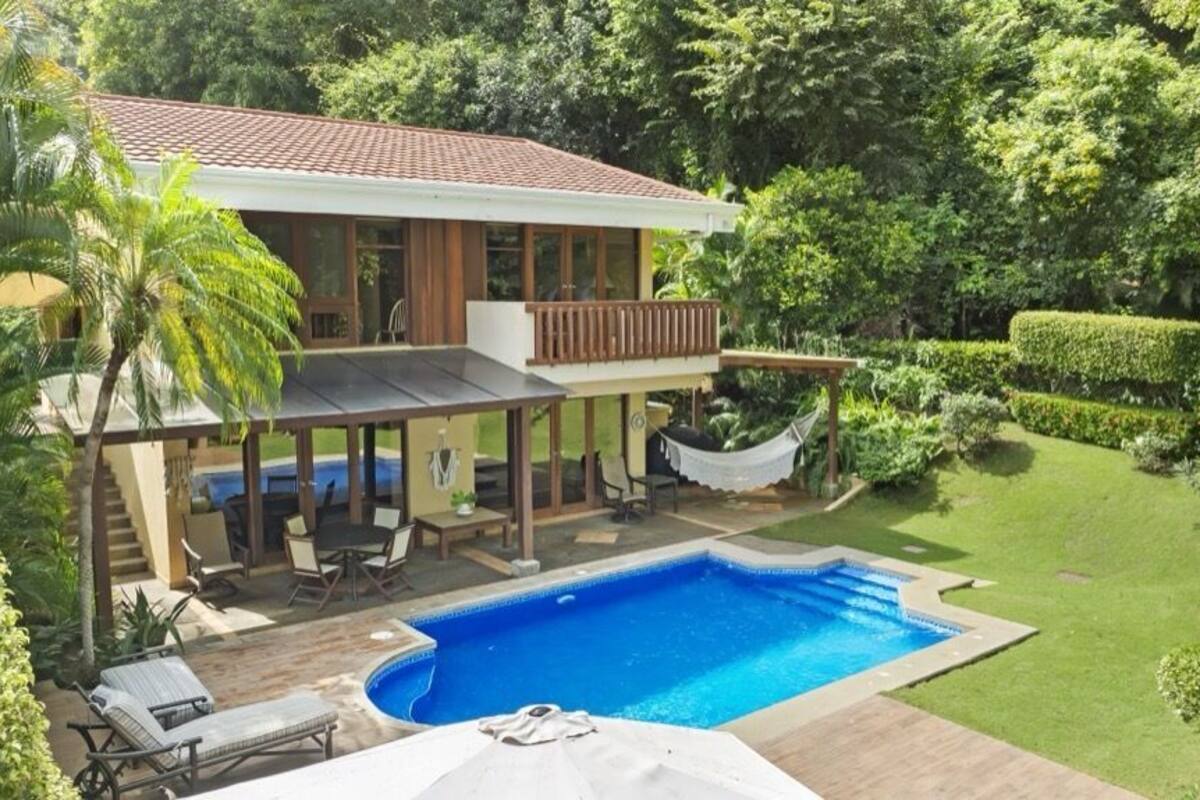 Ein zweistöckiges Haus mit Swimmingpool, Gartenmöbeln und einer Hängematte.