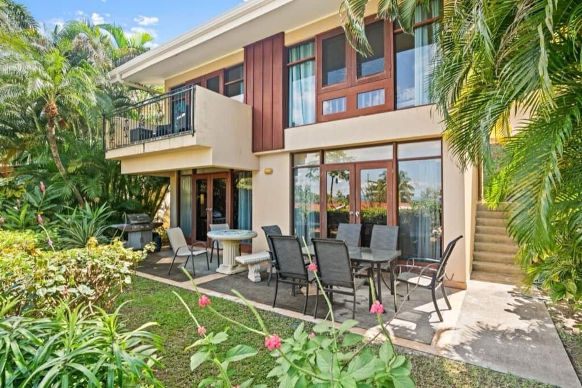 Ein zweistöckiges Haus mit Balkon, Sitzgelegenheit im Freien und üppigem Garten.