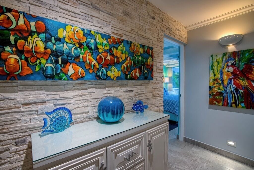 A room with a stone wall and a vibrant fish mural. There is a glass cabinet with decorative items on top.