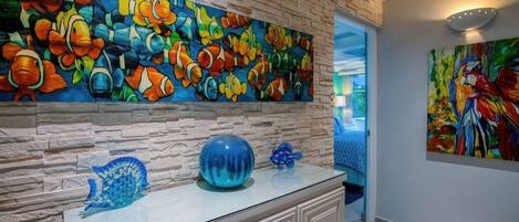 A room with a stone wall and a vibrant fish mural. There is a glass cabinet with decorative items on top.