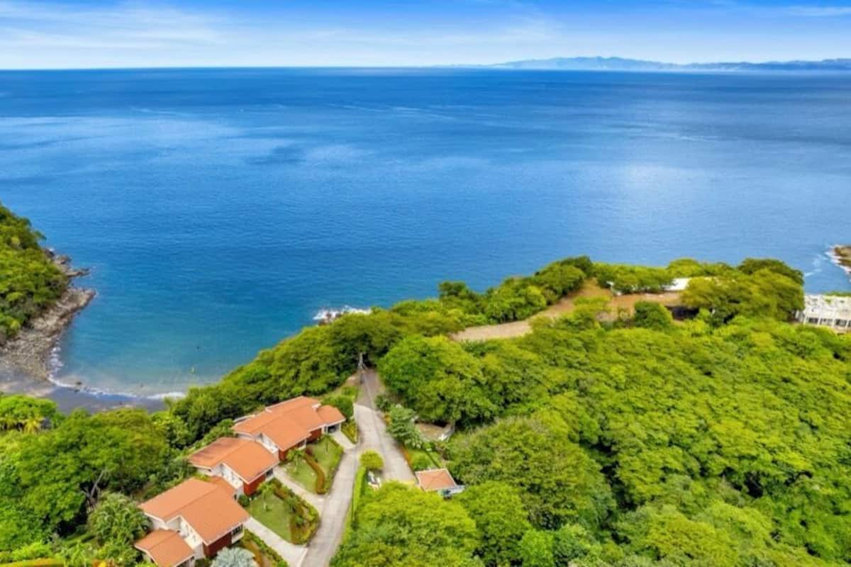 Eine Luftaufnahme einer Küstenregion mit üppigem Grün, blauem Meer und einigen Gebäuden mit roten Dächern.