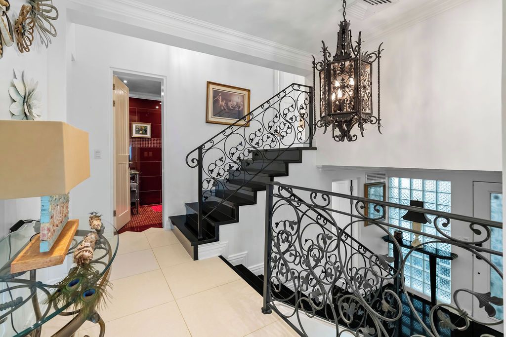 A staircase with ornate metal railings, a chandelier, and a glass table with decorative items.