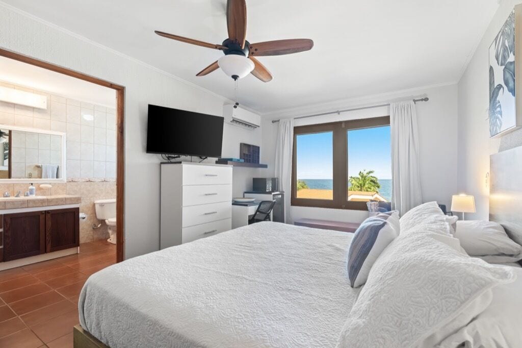 A hotel room with a bed, a desk, a television, and a view of the ocean.