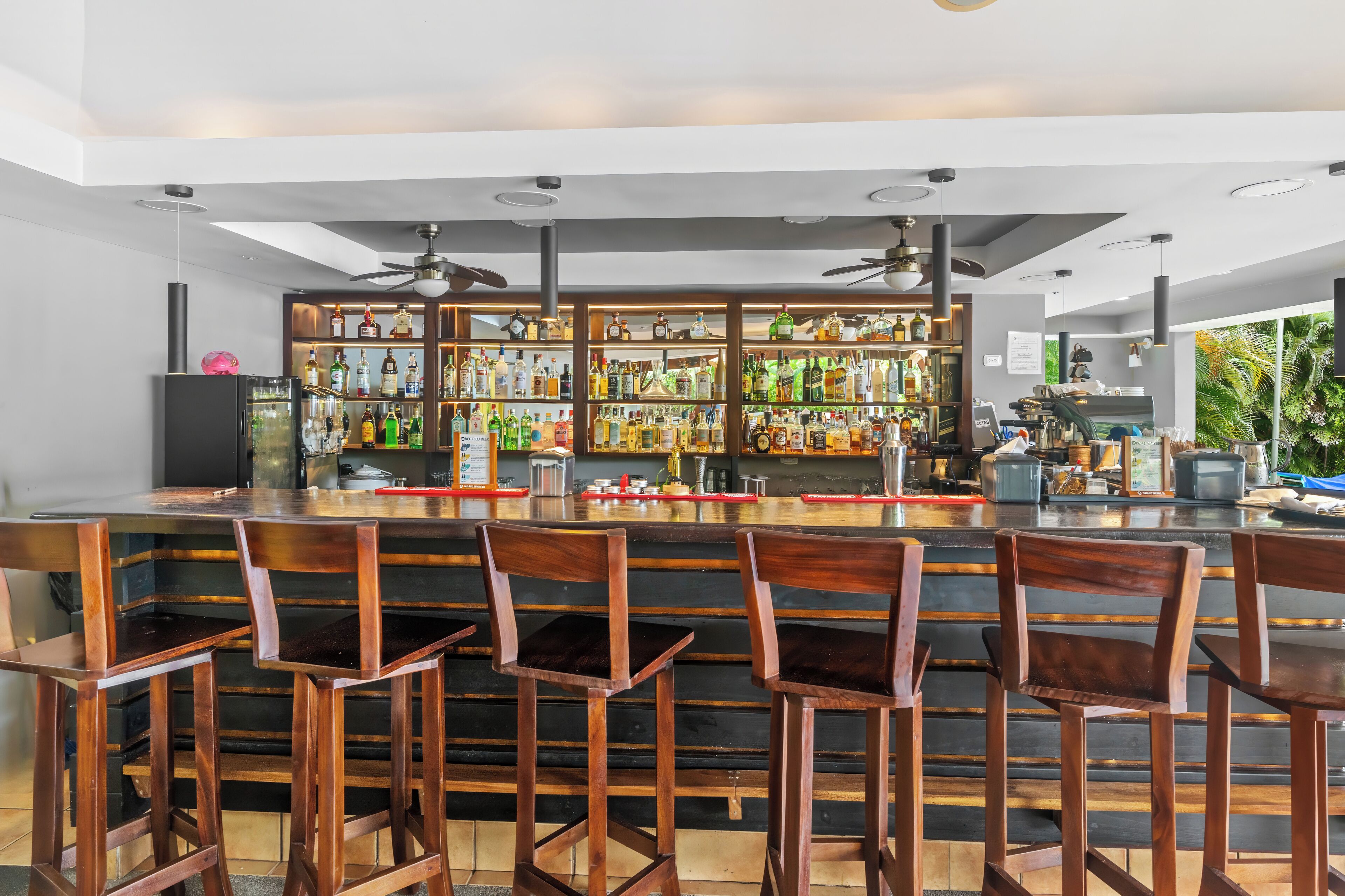 Una zona de bar con taburetes de madera, diferentes botellas de licores en estanterías y una máquina de café.