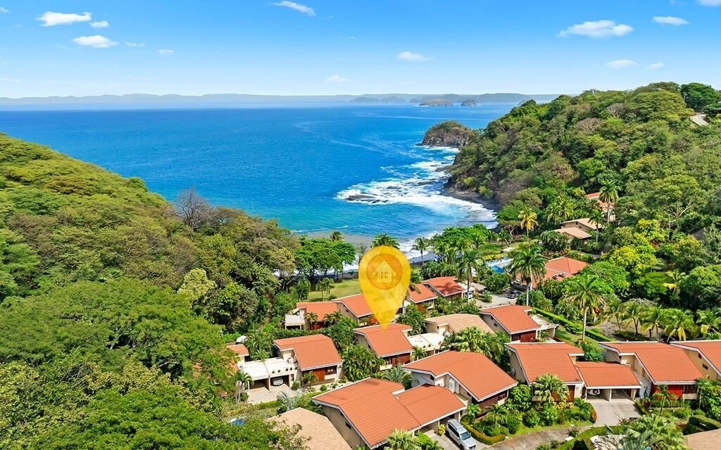 A coastal residential area with houses, lush greenery, and a view of the ocean.