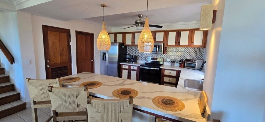 A modern kitchen with a central island, wooden cabinets, and pendant lighting.