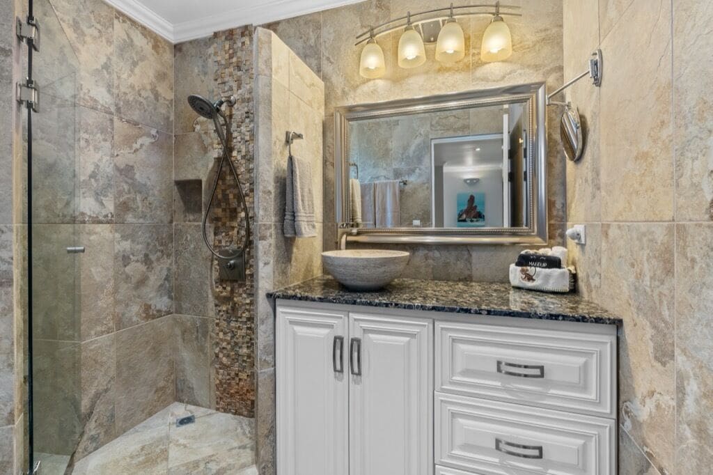 A bathroom with a stone shower, a large mirror, and a granite countertop.