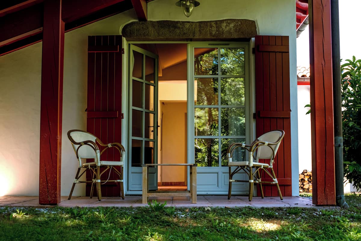 A covered porch with two wicker chairs and a glass table, leading to a door with a view of the outdoors.