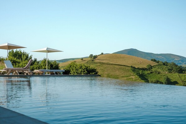 A pool area with lounge chairs and umbrellas, surrounded by a hilly landscape.
