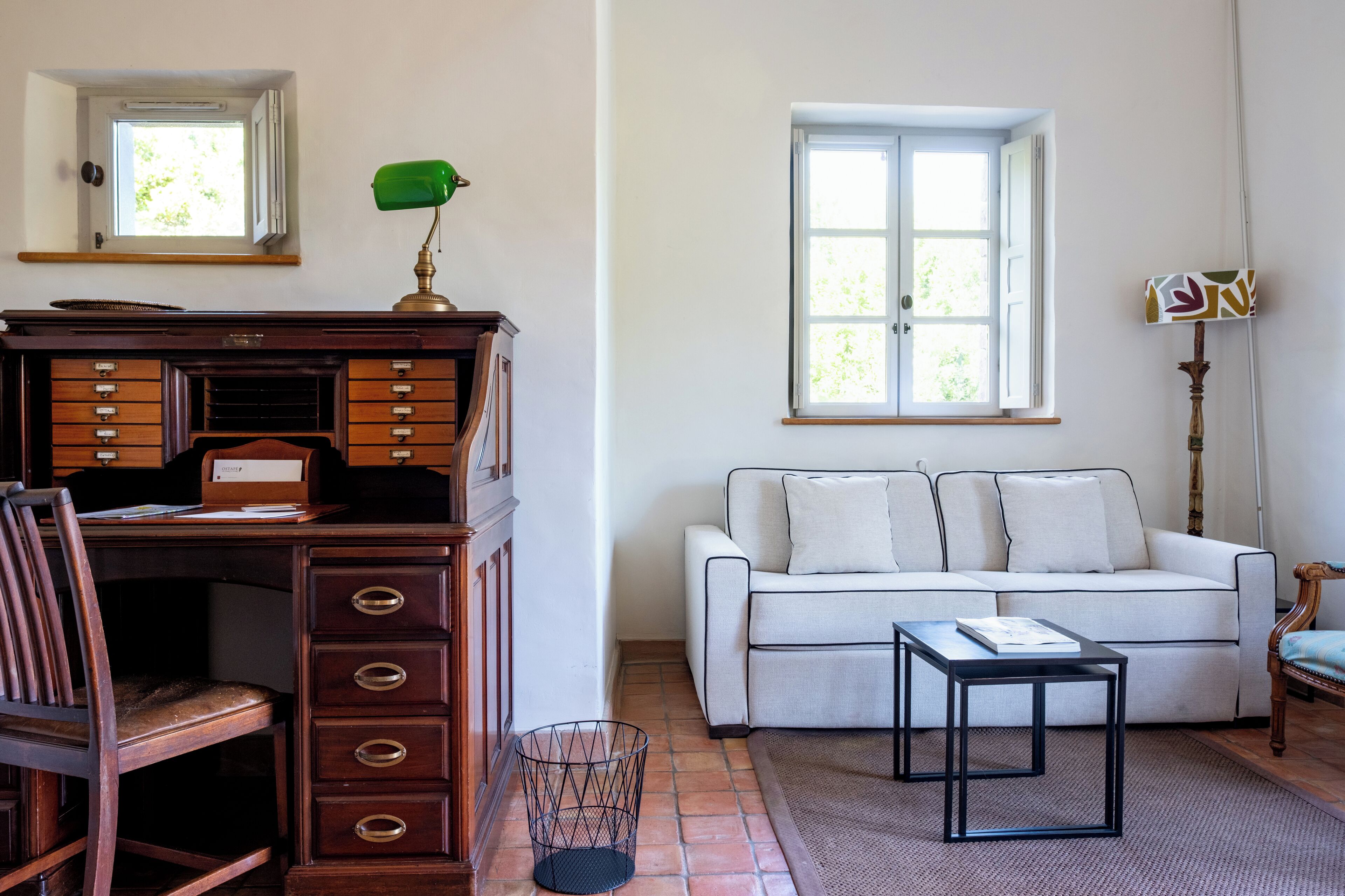 Une pièce avec un bureau en bois, un canapé blanc, une petite table et une fenêtre avec des rideaux.