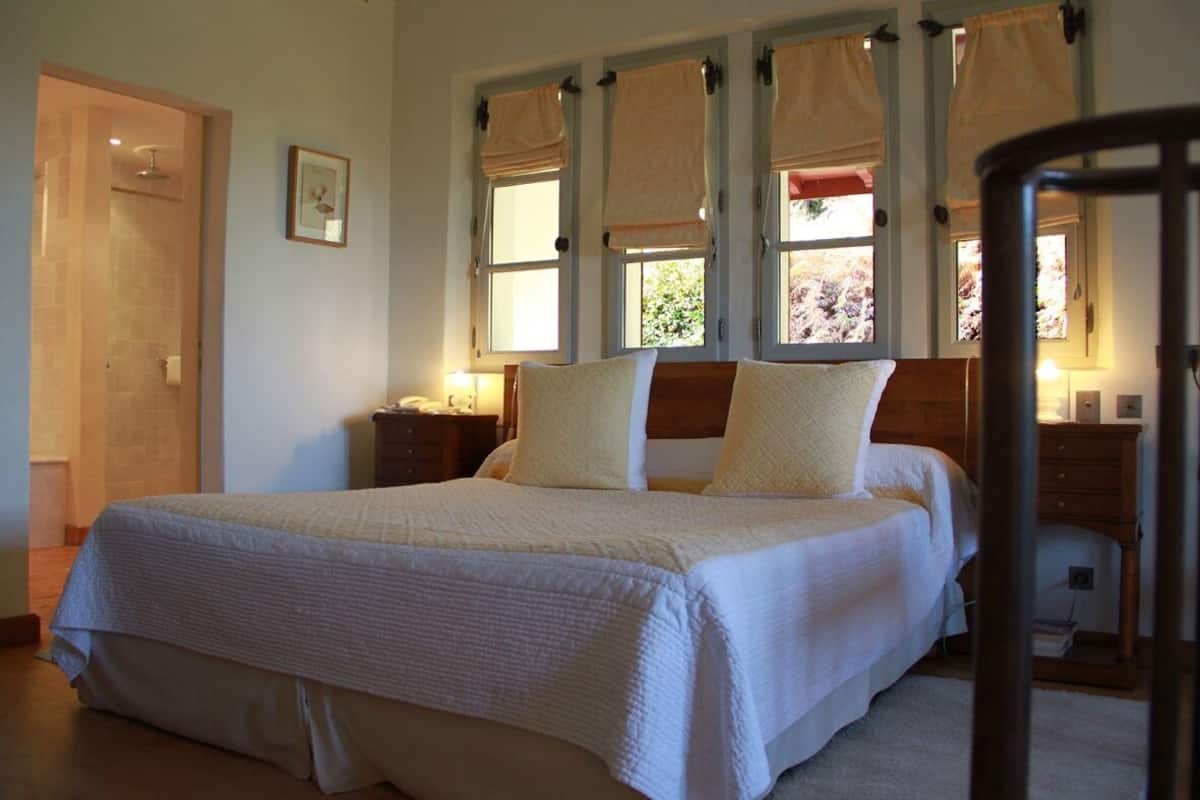 A bedroom with a large bed, a wooden headboard, a nightstand, a bedside table, and a window with curtains.