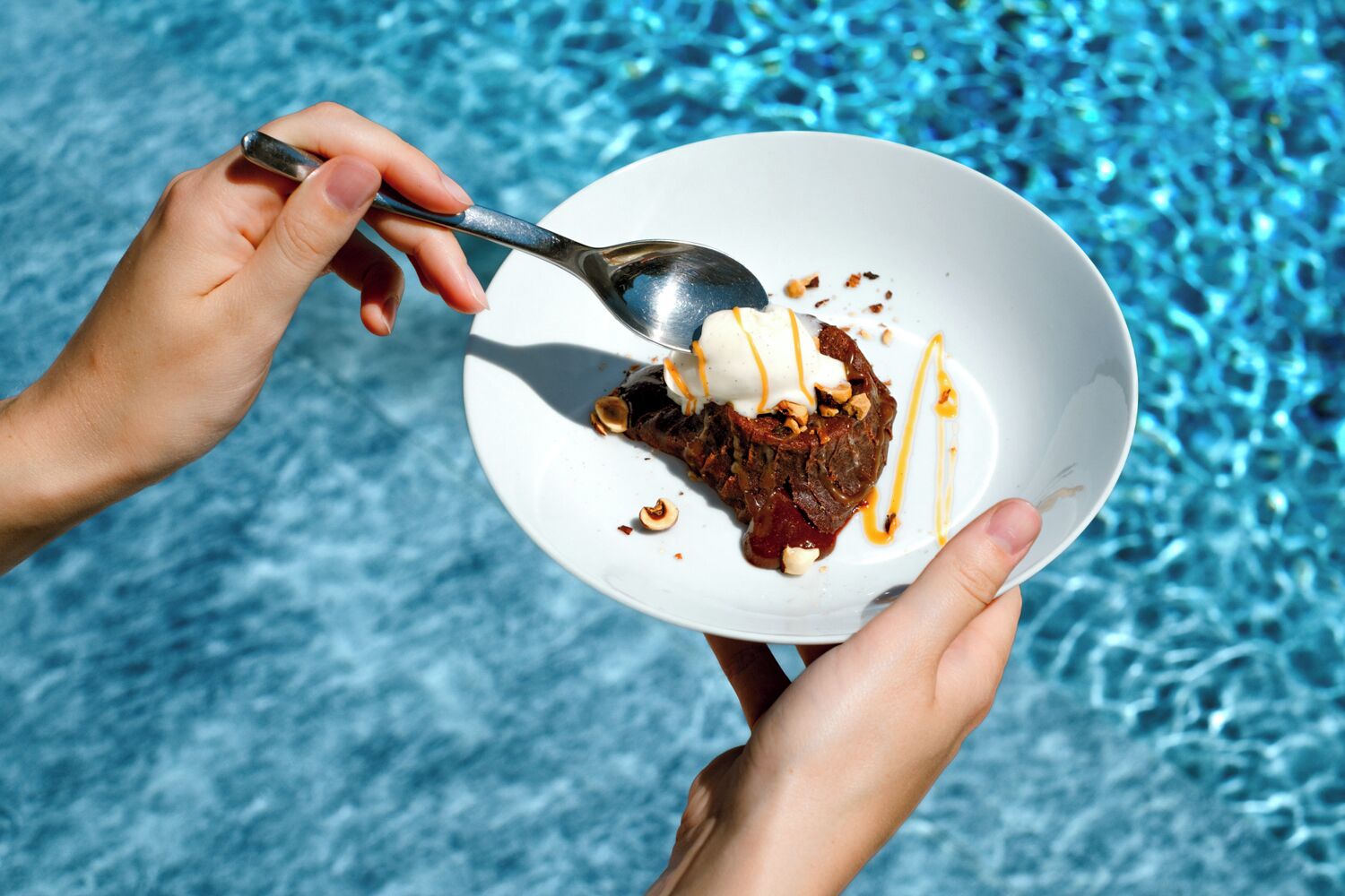 A person holding a white plate with a dessert and a spoon.