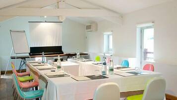 A conference room with a long table, colorful chairs, a whiteboard, and a projector screen.