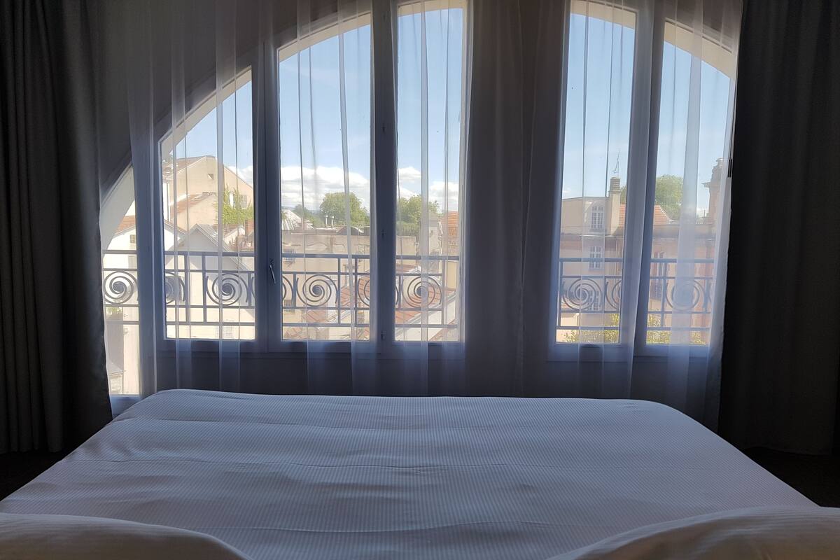 A hotel room with a large window, a bed, and a view of the cityscape.