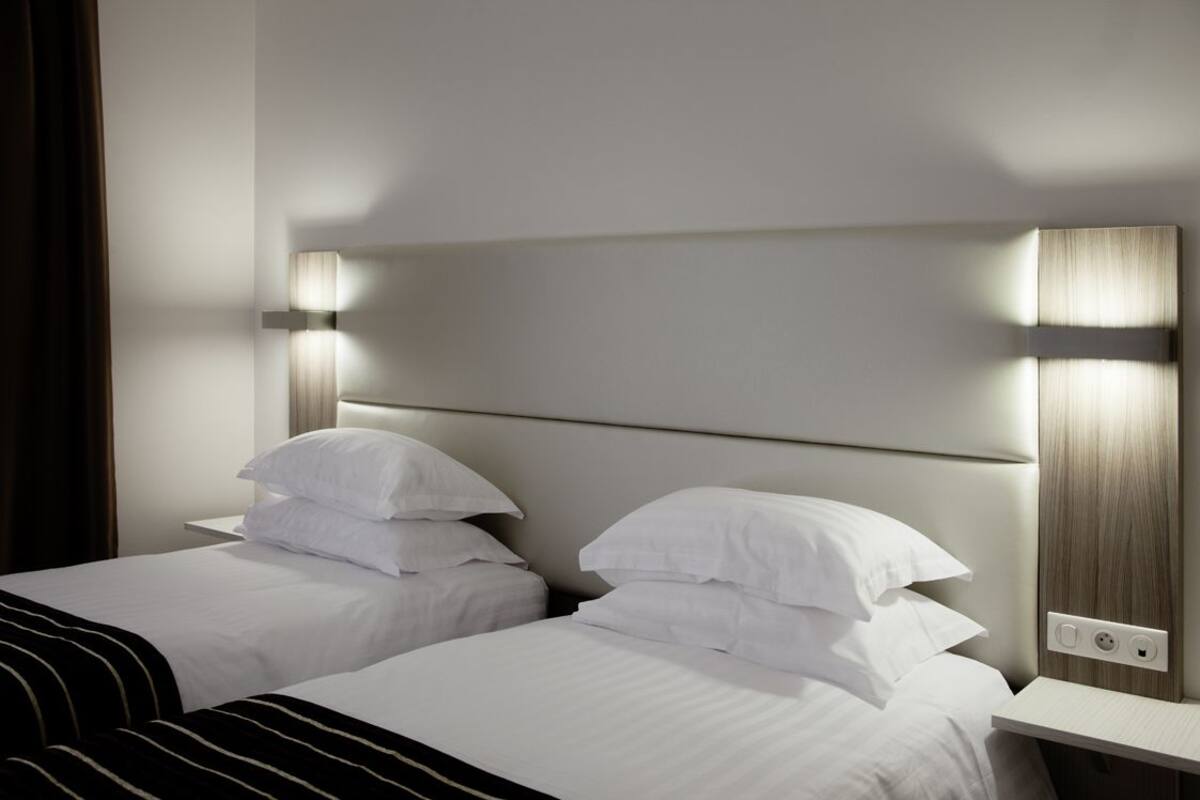 A hotel room with two beds, each with white linens and pillows, a wooden headboard, and bedside lamps.