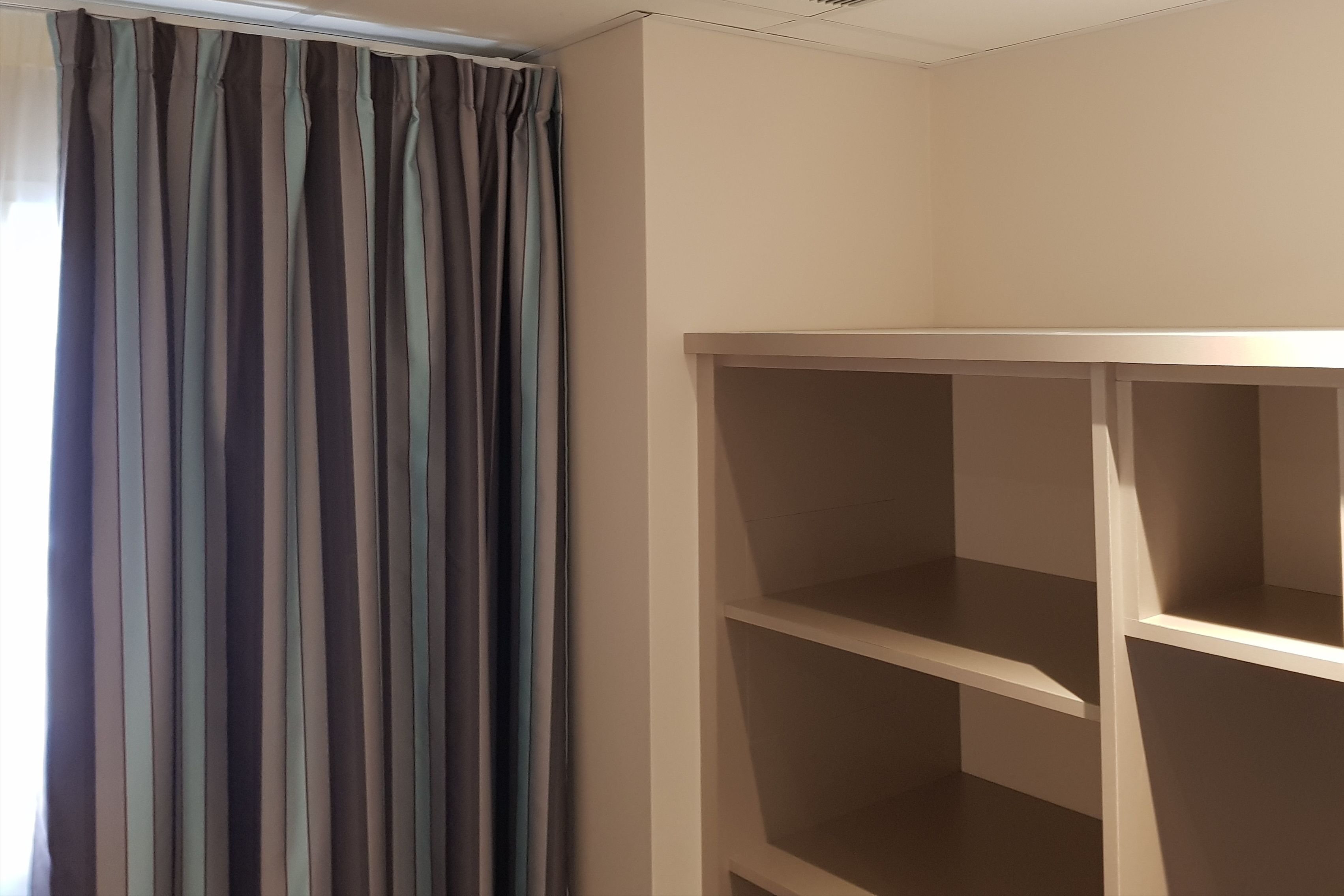 A room with a striped curtain, a white wall, and a built-in shelving unit.