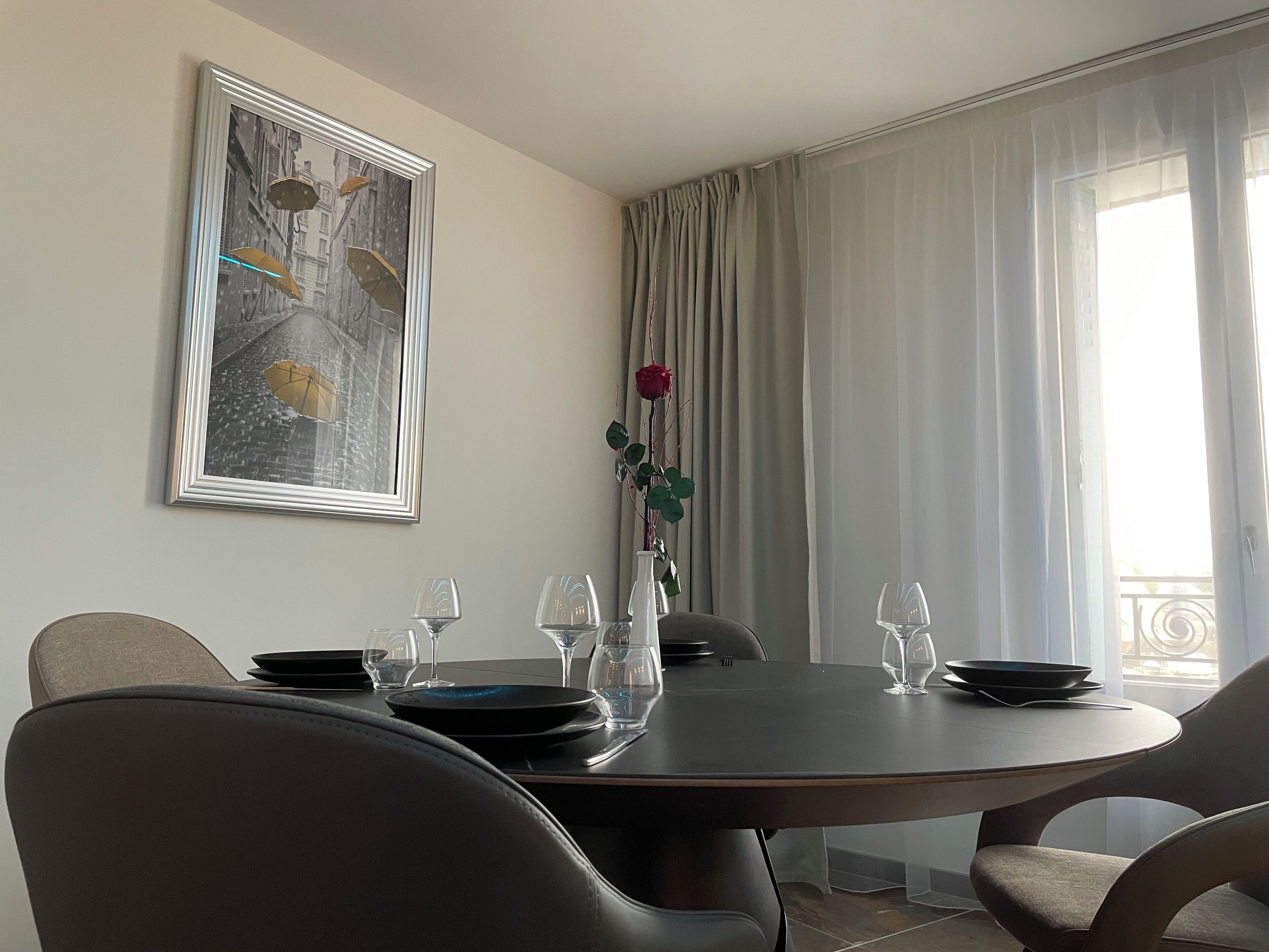 Un comedor con una mesa redonda dispuesta para cuatro personas, un cuadro en la pared y una ventana con cortinas.