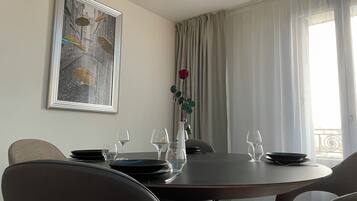 Un comedor con una mesa redonda dispuesta para cuatro personas, un cuadro en la pared y una ventana con cortinas.