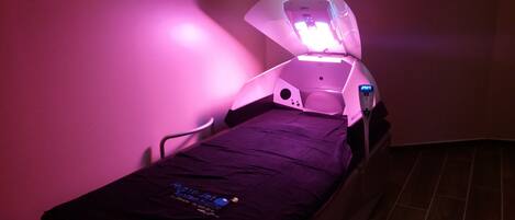 A treatment room with a bed, a ceiling-mounted device, and a control panel.
