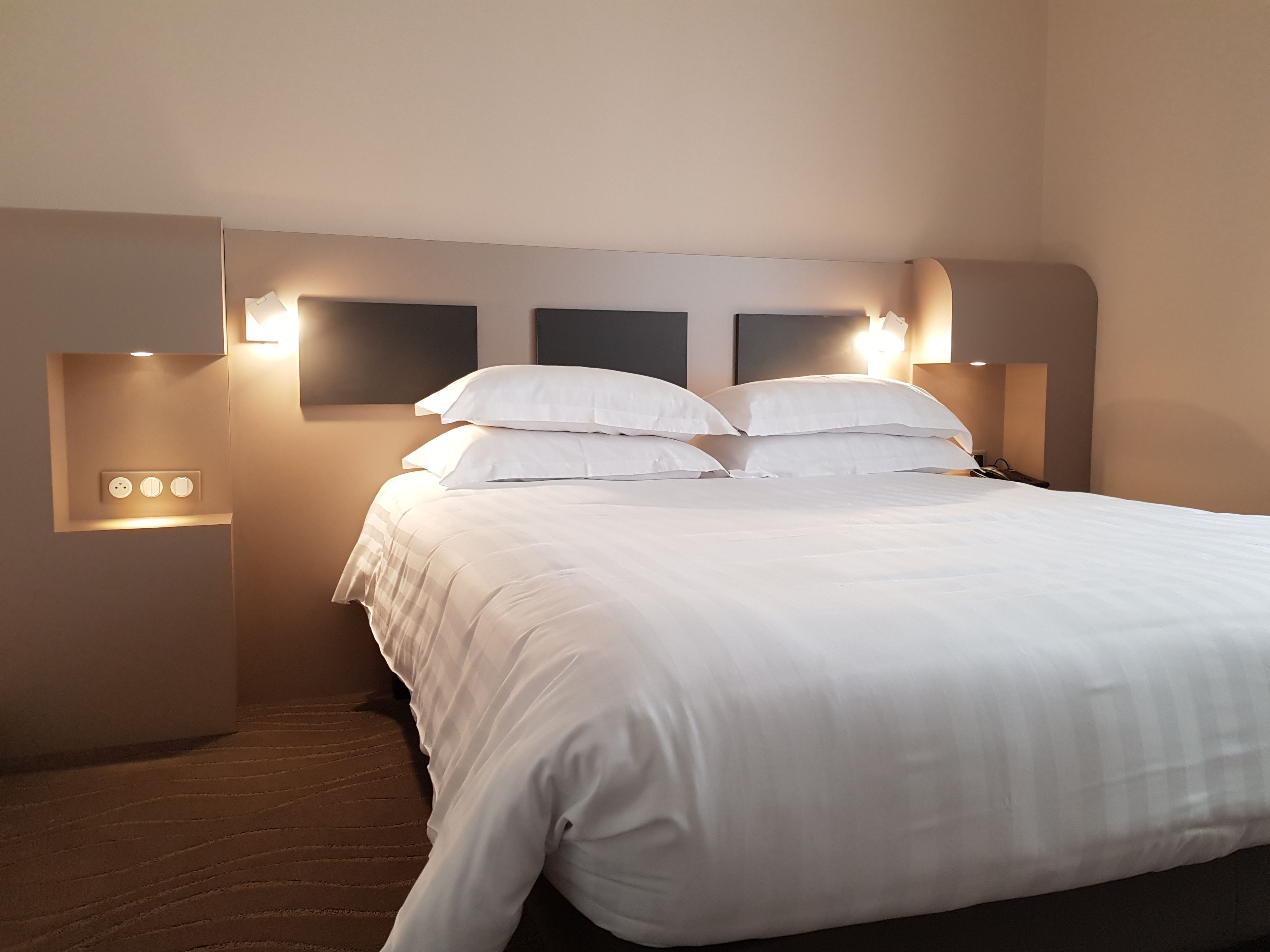 A neatly made bed with white linens in a hotel room.