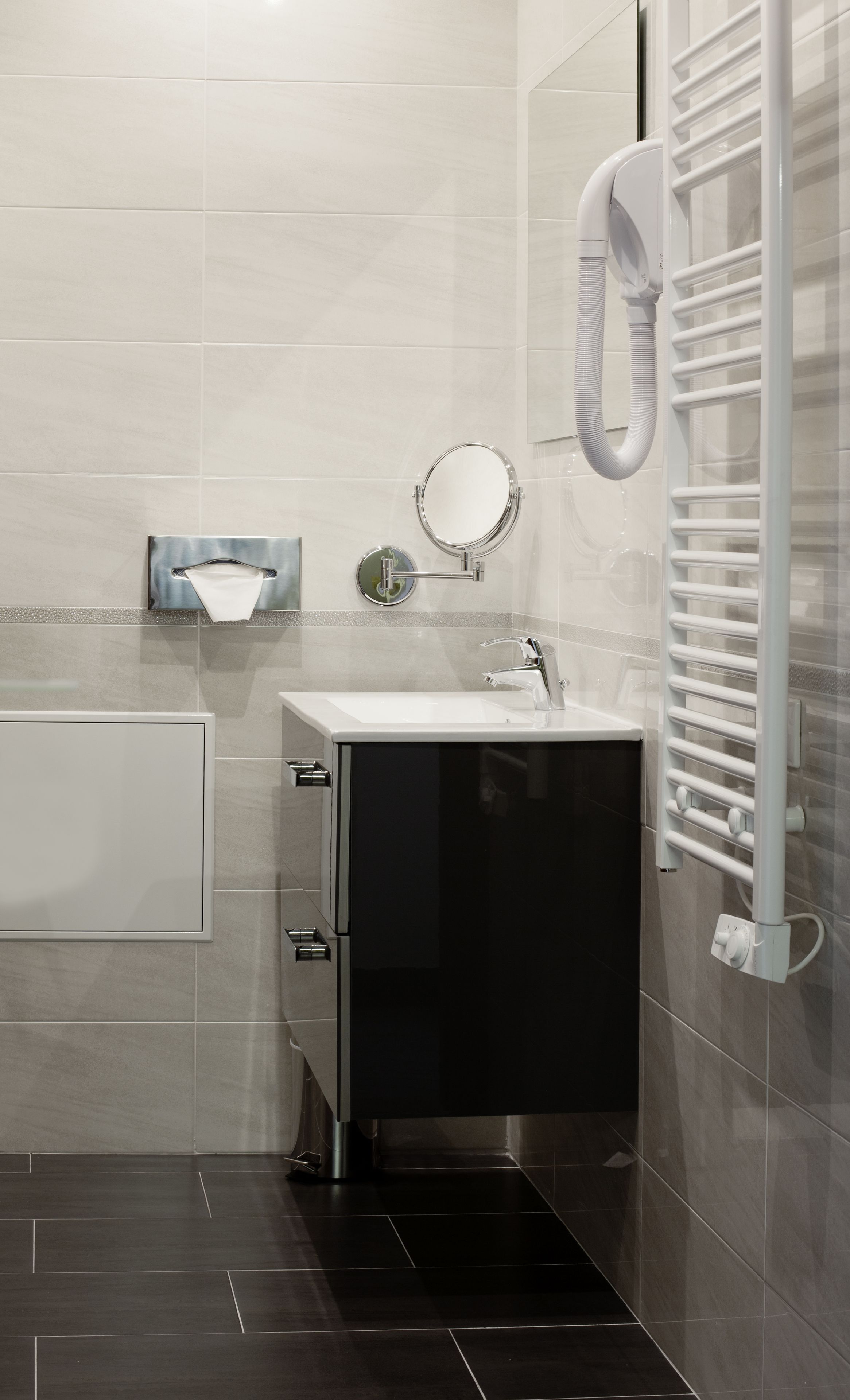 A modern bathroom with a black cabinet, a round mirror, a towel rack, and a built-in heater.