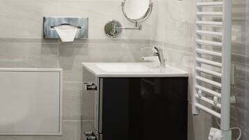 A modern bathroom with a black cabinet, a round mirror, a towel rack, and a built-in heater.