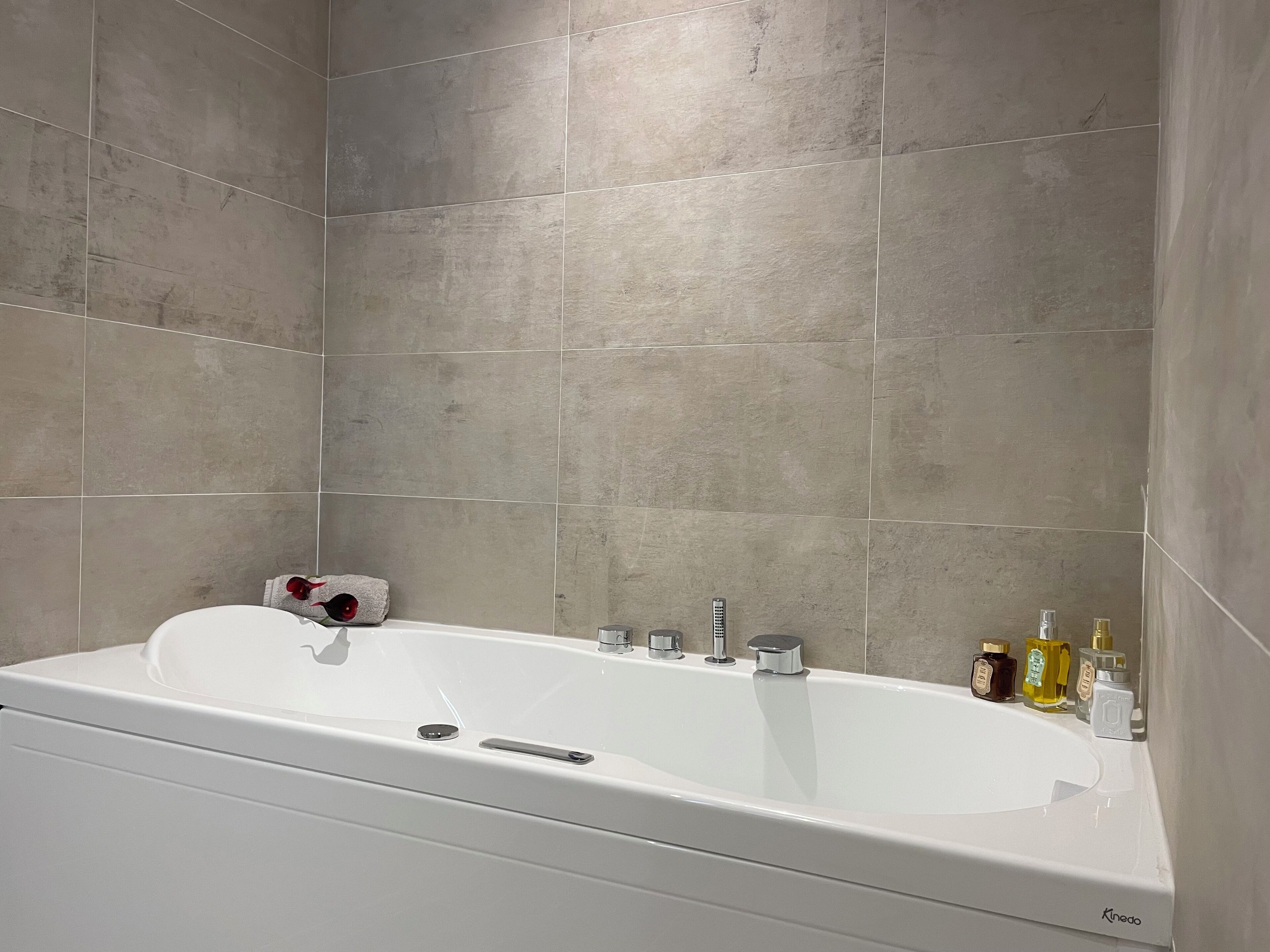 Un baño moderno con una bañera blanca, una toalla y varios artículos de aseo en el borde.