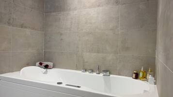 Un baño moderno con una bañera blanca, una toalla y varios artículos de aseo en el borde.